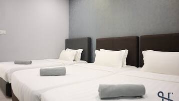A hotel room with three beds, each with white bedding and grey towels.