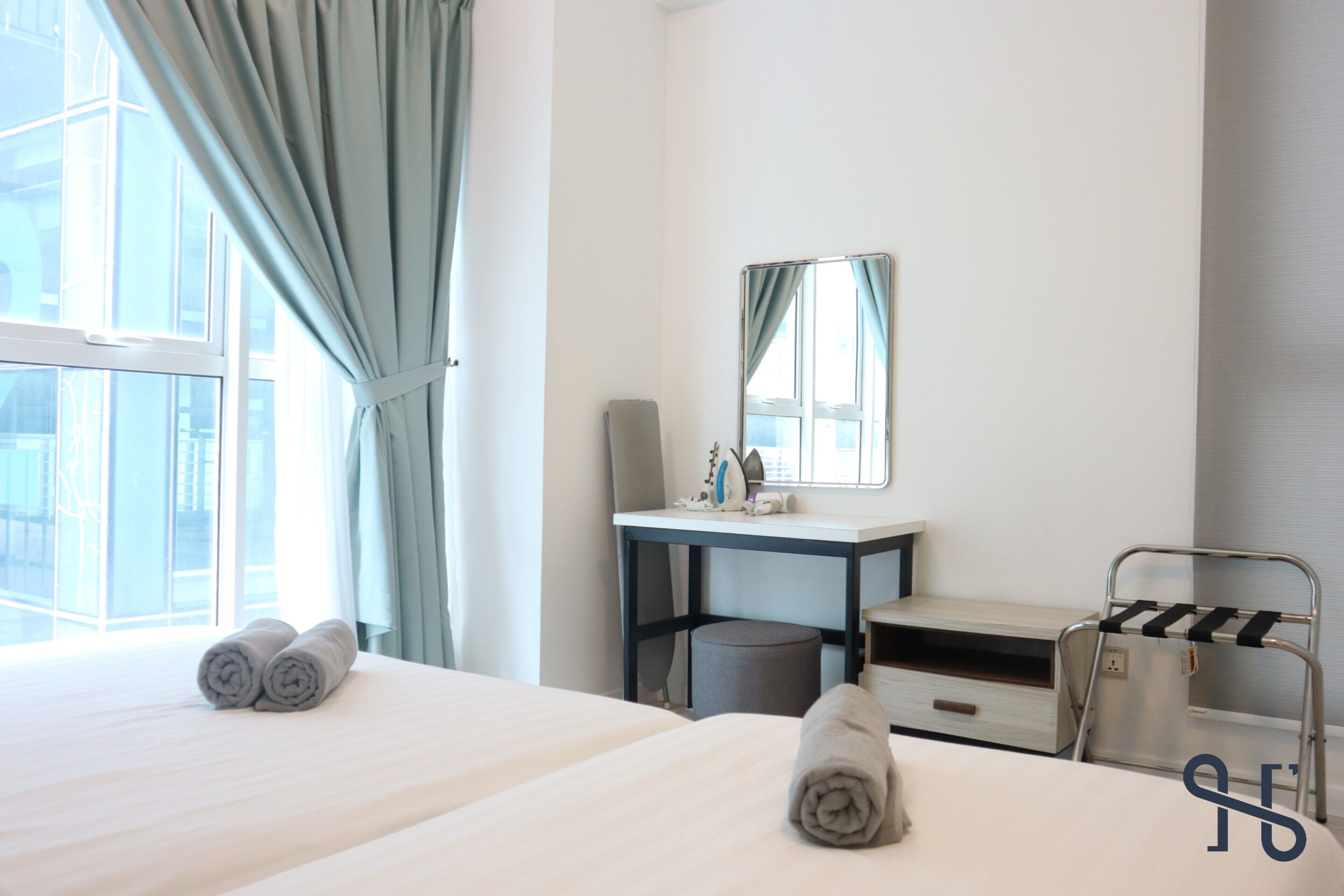 A hotel room with two beds, a desk, a mirror, a towel rack, and a window with curtains.