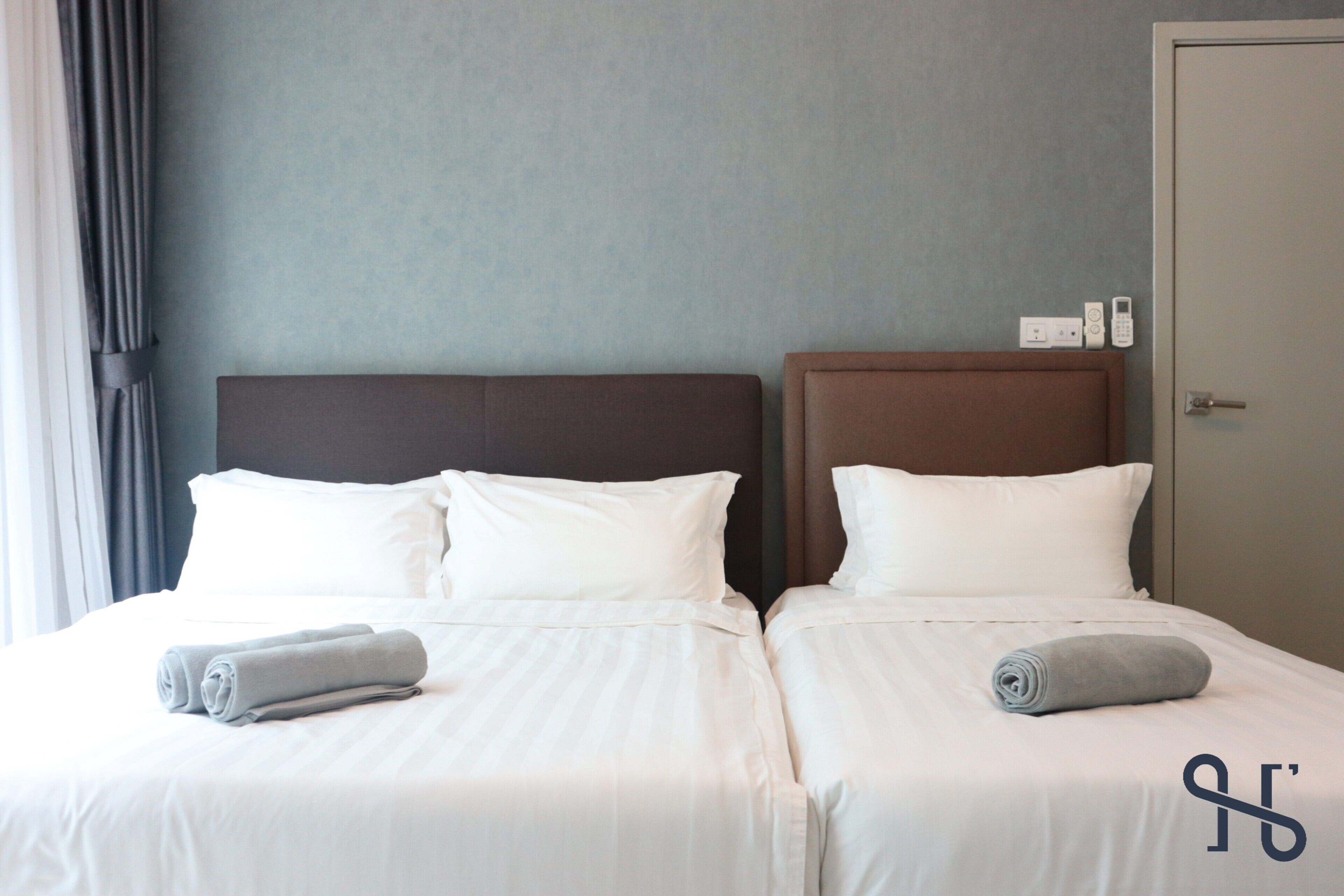 A double bed with white linens and two rolled towels.