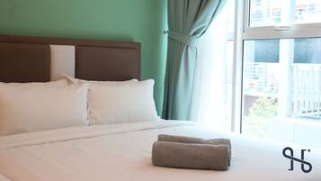 A hotel room with a bed, white bedding, a headboard, and a view of buildings through a window.