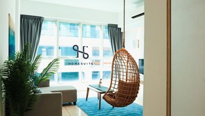 A modern living room with a hanging chair, a sofa, a coffee table, and a large window with curtains. - Homesuite' Home at Sutera Avenue (Kota Kinabalu)