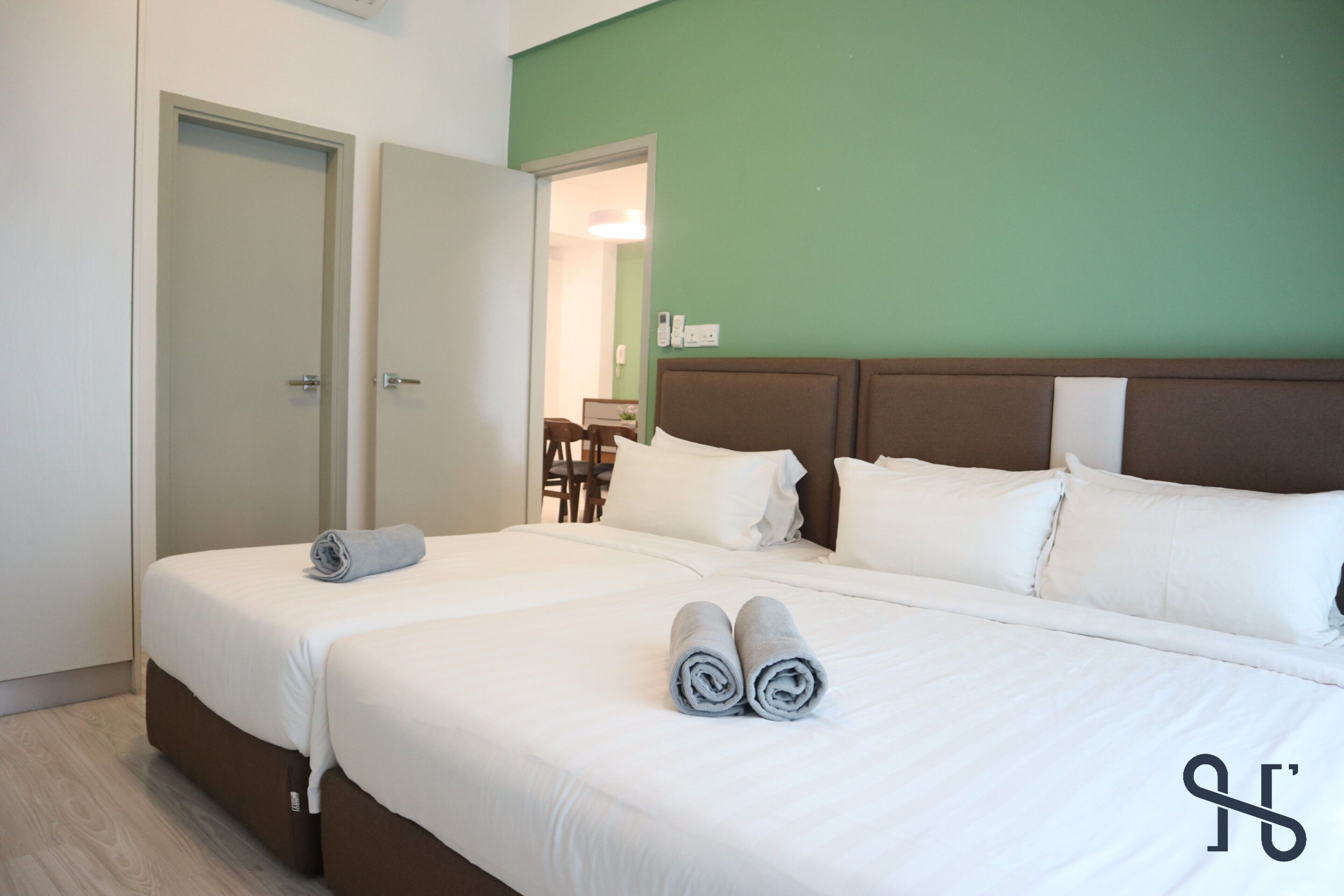 A hotel room with two beds, a green accent wall, and a visible bathroom door.