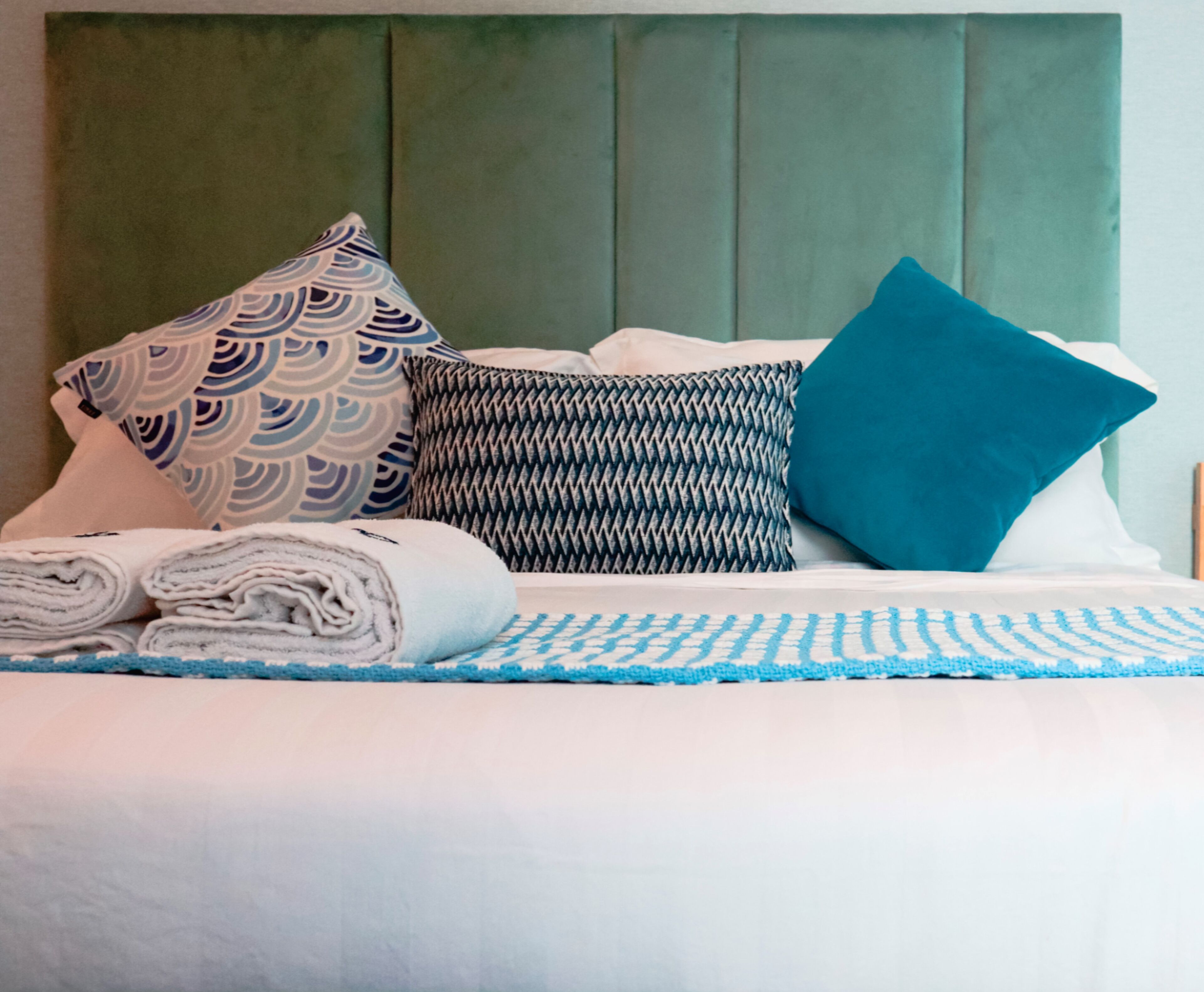 A neatly made bed with patterned pillows and a rolled white towel.