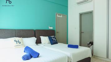 A hotel room with a teal accent wall, a grey headboard, and a white bed with blue towels and pillows.
