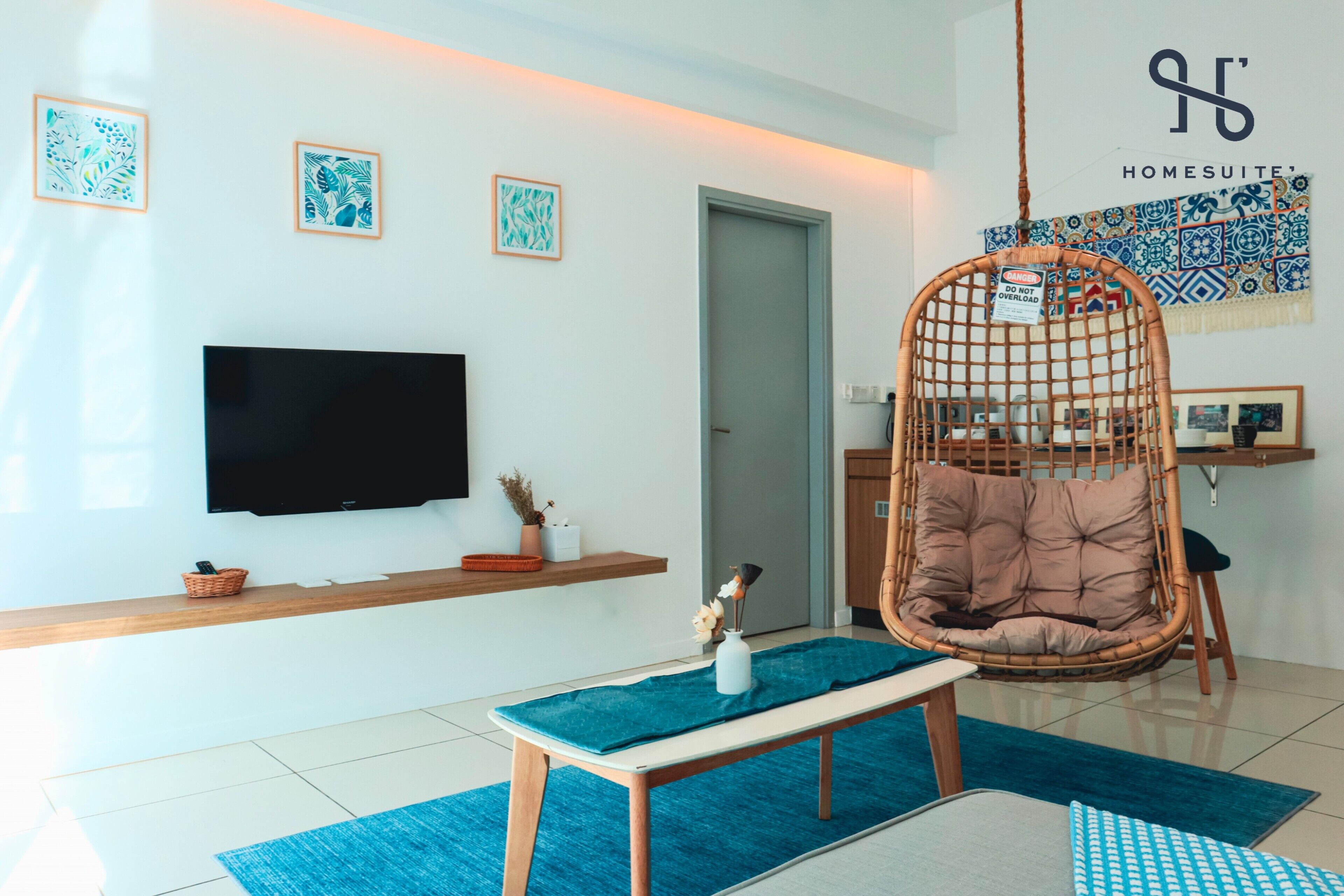 A modern living room with a flat-screen TV, a wicker chair, a bench, and a blue rug.