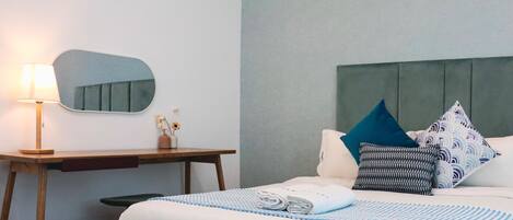 A hotel room with a bed, a desk, a mirror, and a green ottoman.