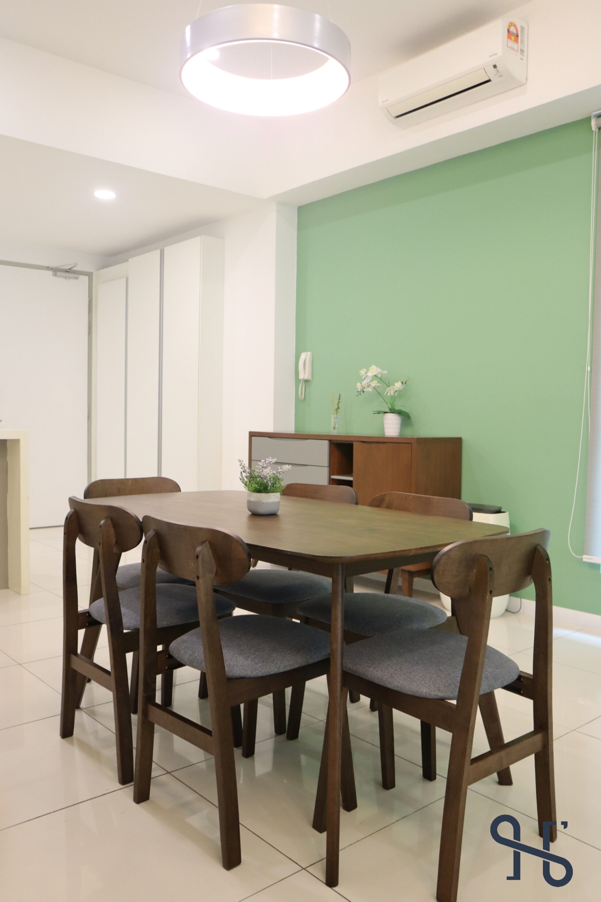 A dining area with a round table, six wooden chairs, a potted plant, and a cabinet against a green wall.