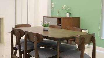 A dining area with a round table, six wooden chairs, a potted plant, and a cabinet against a green wall.