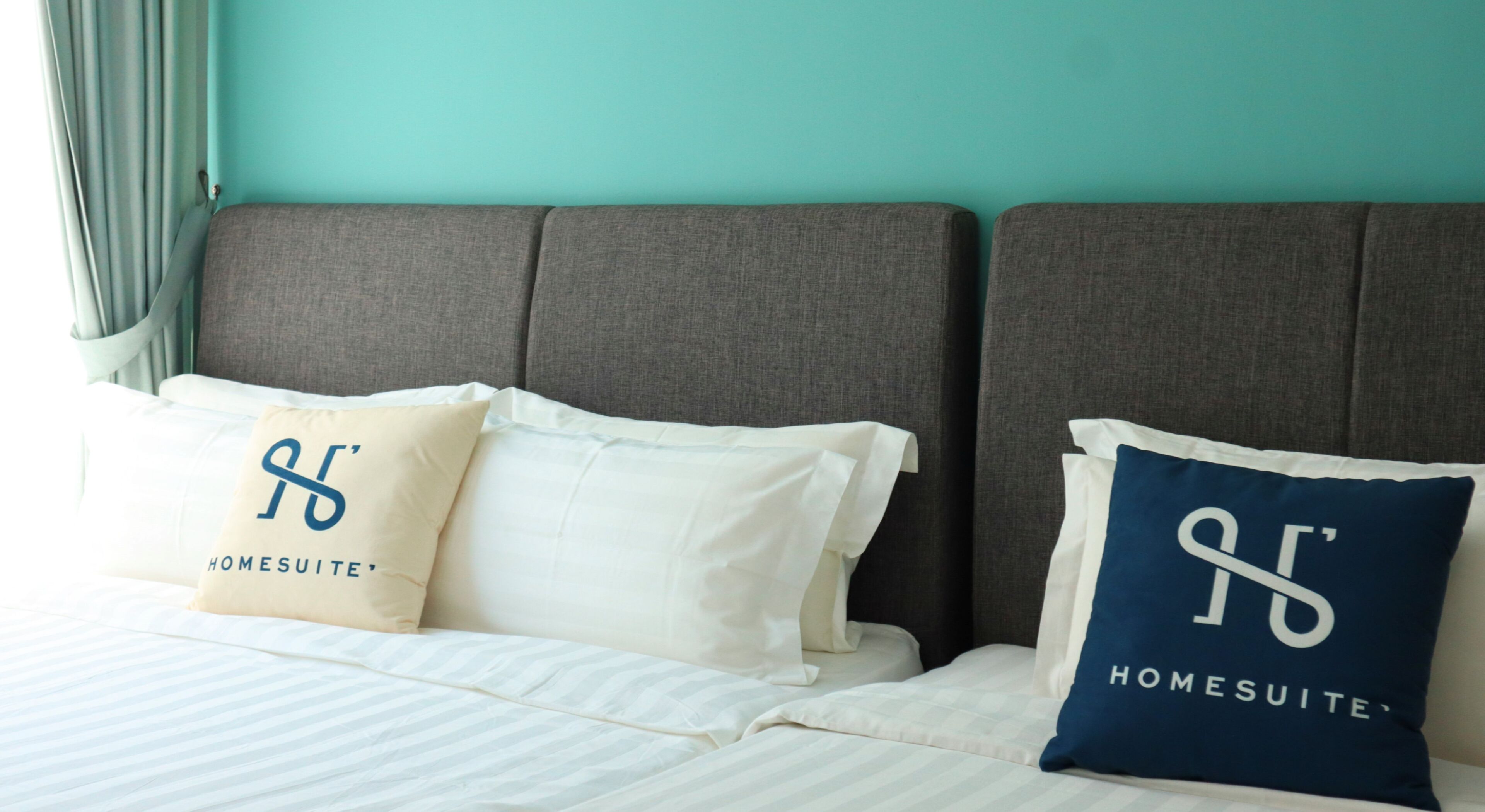A bed with two pillows, one beige and one blue, both with 'HOMESUITE' text.