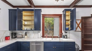 Una cocina con armarios azul oscuro, un lavavajillas de acero inoxidable y una ventana con vista a árboles.