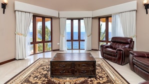 Une pièce spacieuse dotée d’une grande fenêtre donnant sur la mer, d’un fauteuil inclinable en cuir, d’une commode en bois et d’un tapis à motifs.