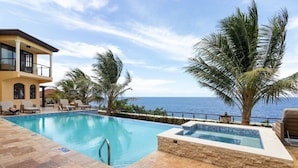 Un espace piscine avec vue sur la mer, un bâtiment à deux étages et des palmiers.