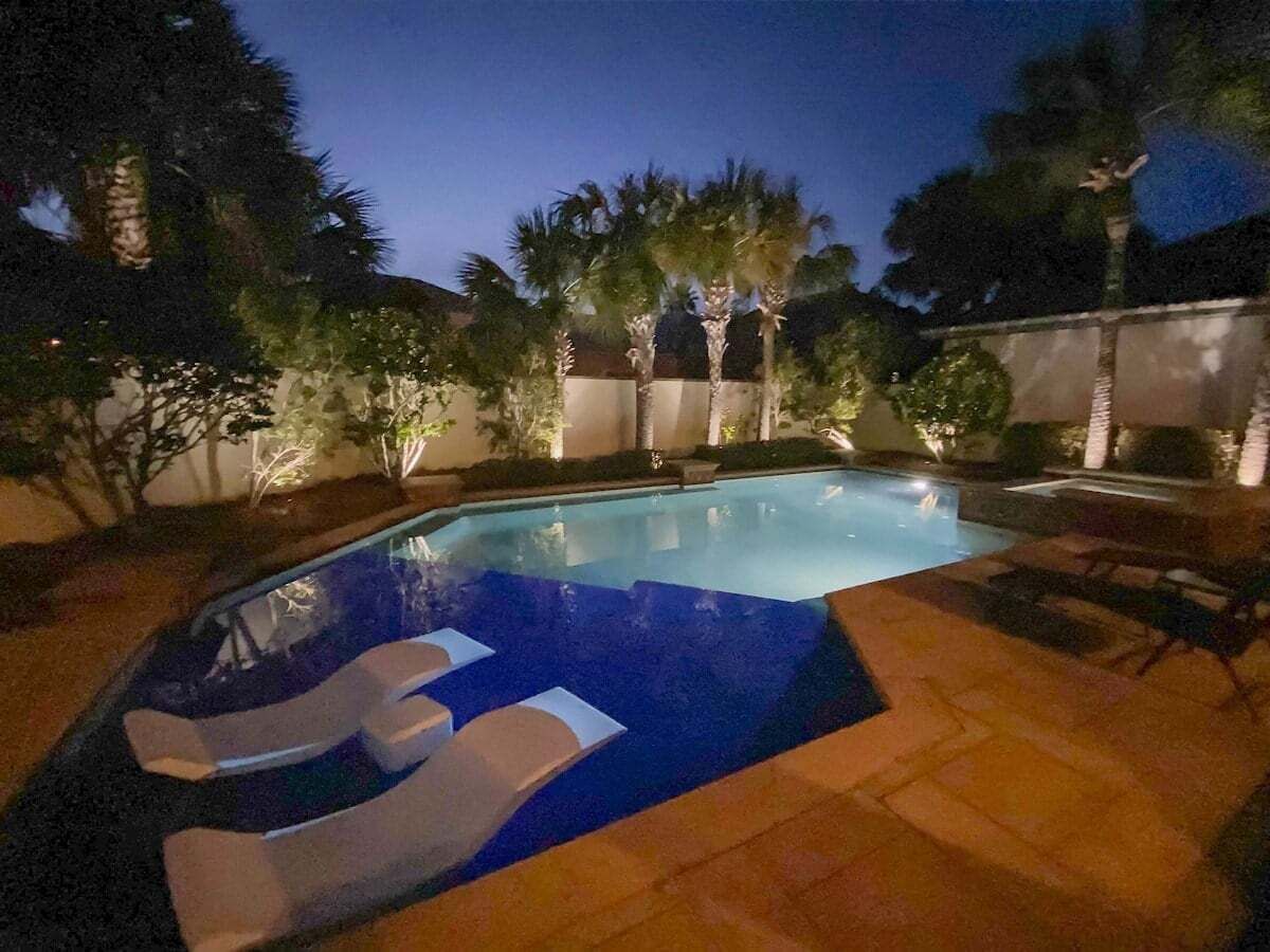 Une piscine aux motifs de mosaïque bleus, entourée de palmiers et dotée d’une terrasse carrelée.