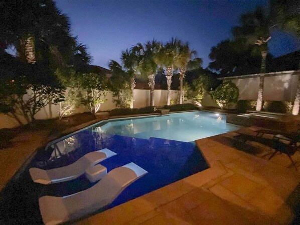 A swimming pool with a blue mosaic design, surrounded by palm trees and a tiled deck.