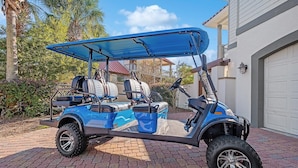 A golf cart parked on a paved driveway with a house in the background.