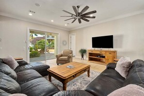 A living room with a leather sofa, a wooden coffee table, a television on a wooden stand, and a ceiling fan.