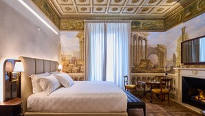 A spacious bedroom with a large bed, a fireplace, a dining area, and a mural on the wall. - Duomo Luxury Florence (Florence)