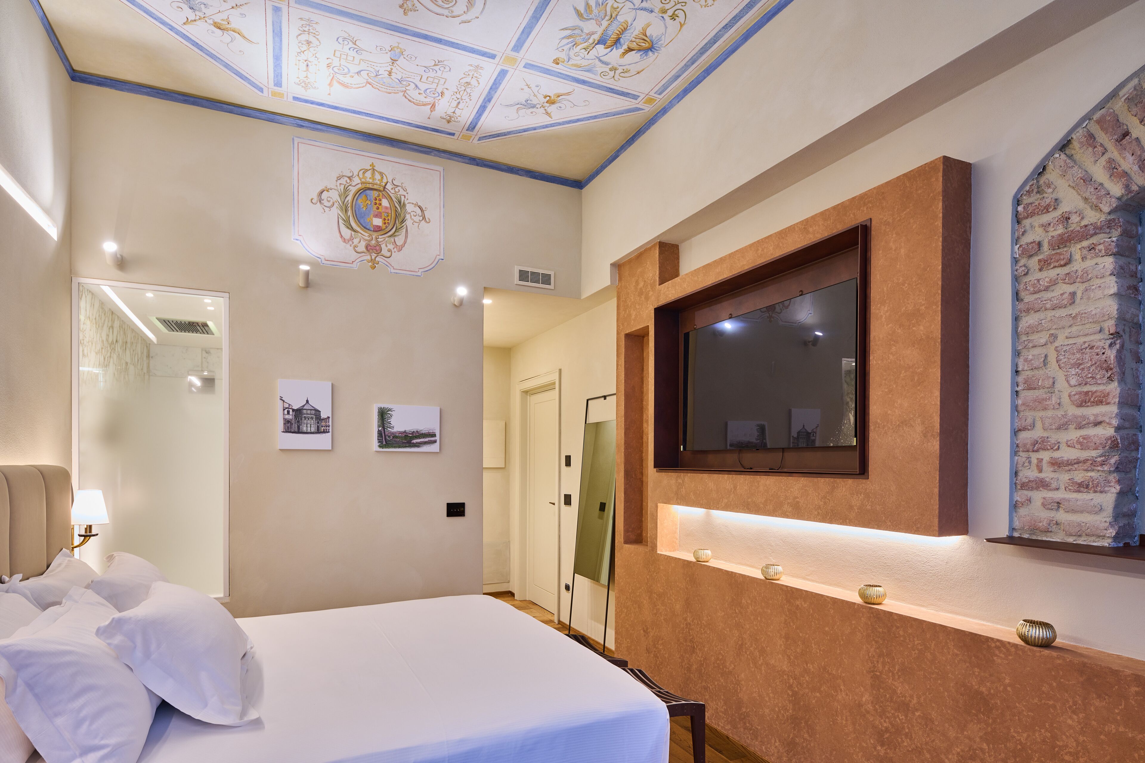 Habitación de hotel con una cama grande, un televisor montado, un espejo y un techo decorativo.