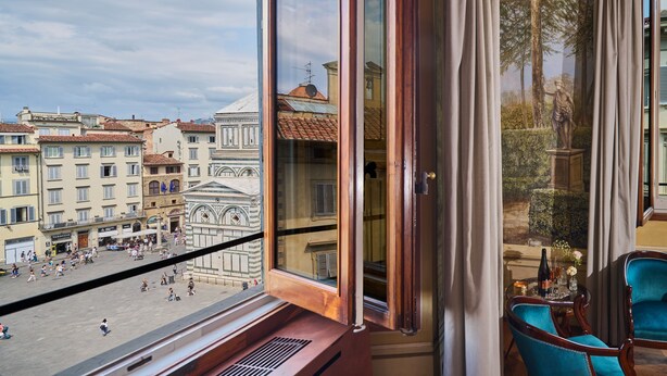A room with a large window overlooking a public square with historic buildings, a statue, and a fountain. - Duomo Luxury Florence (Florence)