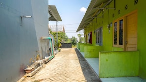 A narrow alleyway with a paved path, flanked by buildings with green and white walls, and a visible door on the right. - SPOT ON 93210 Griya Kos Kanjeng Mami Syariah (Jogoroto)
