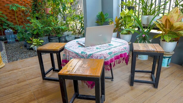A wooden table with a laptop on it, surrounded by potted plants and a patterned tablecloth. - SPOT ON 93210 Griya Kos Kanjeng Mami Syariah (Jogoroto)