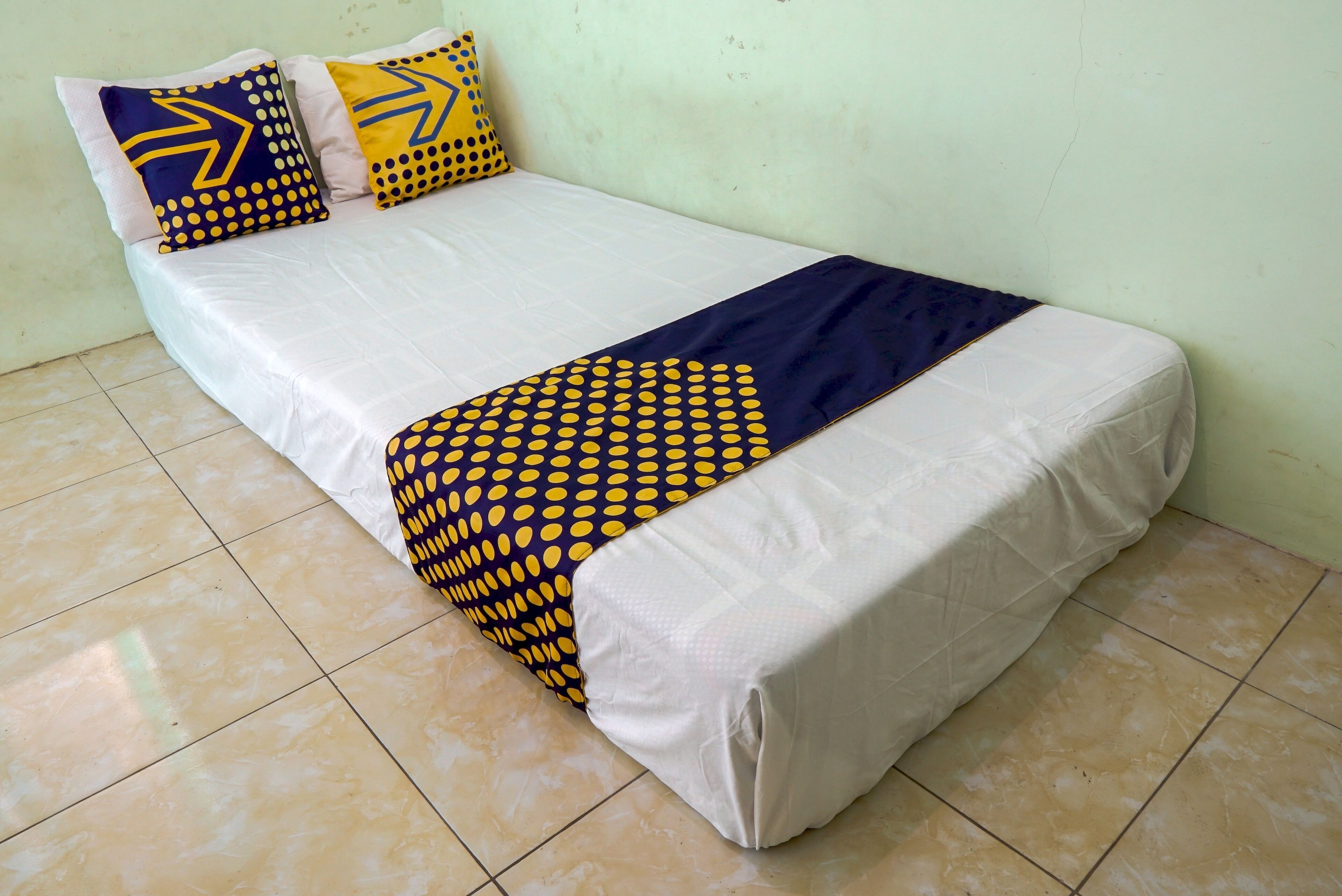 A bed with a white mattress, a navy blue blanket, and patterned pillows.