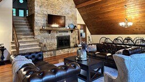 A spacious living area with a stone fireplace, leather sofas, and a wooden ceiling.