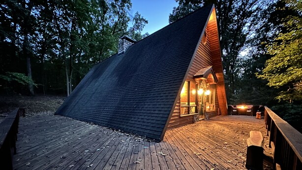 A wooden cabin with a sloped roof, a deck, and a small porch area with seating.