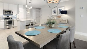 Eine moderne Küche mit Edelstahlgeräten, einem Holzespeisetisch mit blauen Tischsets und einer Deckenleuchte.