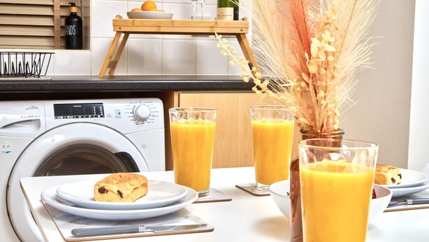 A kitchen with a washing machine, a wooden table with breakfast items, and a vase with dried plants. - Perfect for Family & Corporates - FREE Parking - Contact us for better rates! (Headingley)