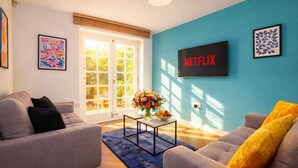 A living room with two sofas, a coffee table, a TV wall-mounted above a sofa, and a door leading to a garden. - Perfect for Family & Corporates - FREE Parking - Contact us for better rates! (Headingley)