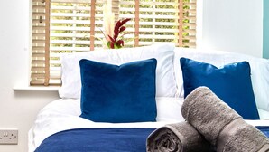 A neatly made bed with blue and white bedding, a rolled towel, and a window with wooden blinds and a plant. - Perfect for Family & Corporates - FREE Parking - Contact us for better rates! (Headingley)