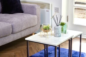 Moderni olohuone, jossa on harmaa sohva, valkoinen marmorinen sohvapöytä sekä koriste-esineitä, kuten lasinen kulho, jossa on kasveja, ja kaksi maljakkoa.
