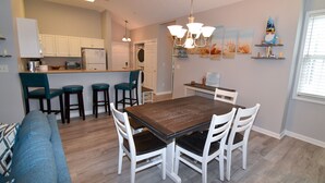 A modern kitchen with white cabinets, a wooden dining table, and a bar area.