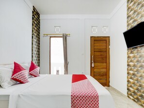 Une chambre d’hôtel avec un lit, une porte en bois, un téléviseur fixé au mur et un papier peint à motifs.