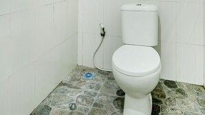 A bathroom with a white toilet, tiled walls, and a floor with a mix of stone and tile patterns. - OYO Flagship 90756 Melasti Hills Room & Cafe (Ungasan)