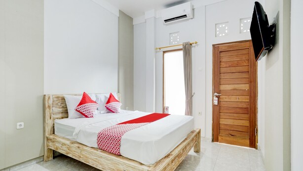 A bedroom with a wooden bed, white walls, a wooden door, and a mounted TV. - OYO Flagship 90756 Melasti Hills Room & Cafe (Ungasan)