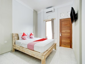 A bedroom with a wooden bed, white walls, a wooden door, and a mounted TV. - OYO Flagship 90756 Melasti Hills Room & Cafe (Ungasan)