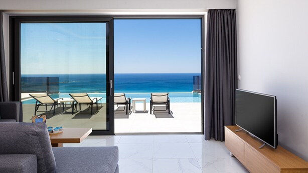 Een moderne woonkamer met een grote televisie, een bank en een balkon met een zwembad en stoelen.