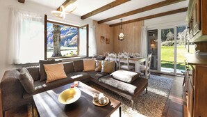 A modern living room with a sectional sofa, a dining table with chairs, and a view of the outdoors. - Casa Mima Chalets (Sonogno)