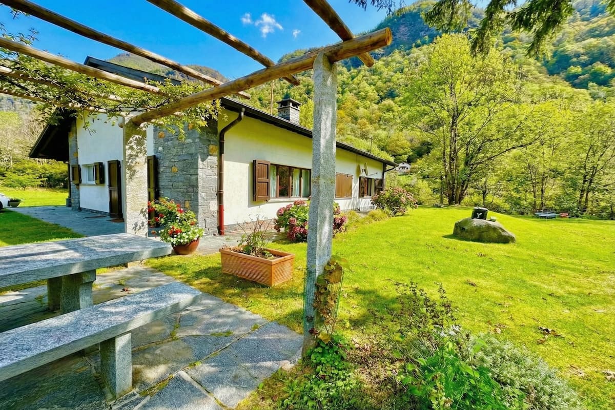 A stone house with a wooden pergola, a stone bench, and a well-maintained lawn.