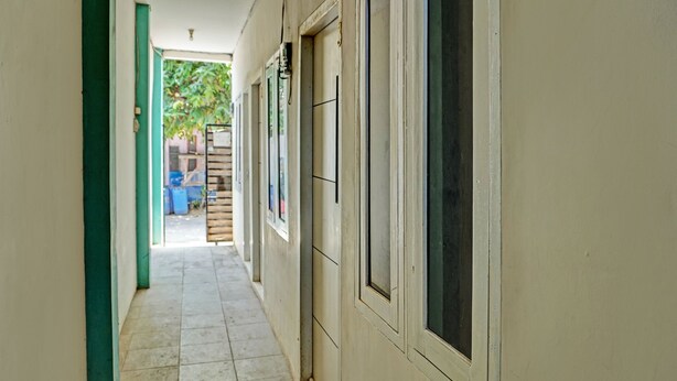 A narrow corridor with tiled flooring, a green door on the left, and windows on the right. - OYO Life 92684 Kost Mutiara Nirwana (Karawang)