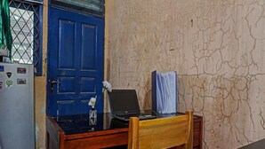 A room with a blue door, a wooden desk with a laptop, and a refrigerator. - OYO Life 92684 Kost Mutiara Nirwana (Karawang)