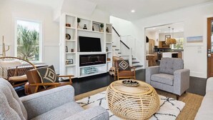 A modern living room with a flat-screen TV, comfortable seating, and a staircase leading to another level. - Folly Oasis | Beachside Home w. Pool + Parking (Folly Beach)