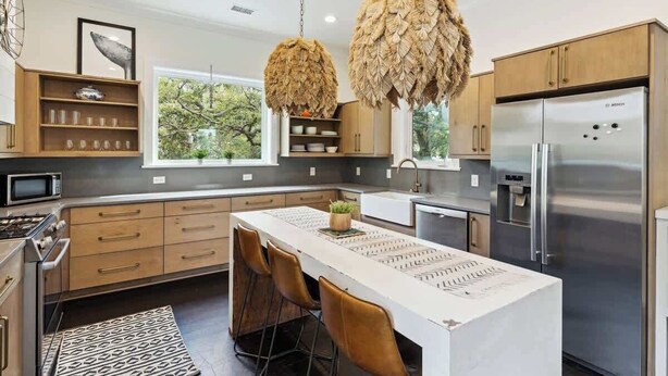 A modern kitchen with wooden cabinets, a stainless steel refrigerator, and a central island with chairs. - Folly Oasis | Beachside Home w. Pool + Parking (Folly Beach)
