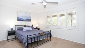 Ein Schlafzimmer mit einem Bett, zwei Nachttischen, einem Deckenventilator, einem Fenster mit Jalousien und einem Wandbild.