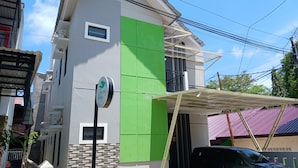 Un bâtiment moderne avec un mur d’accent vert, une enseigne indiquant « Homy Stay », et un espace de stationnement couvert.
