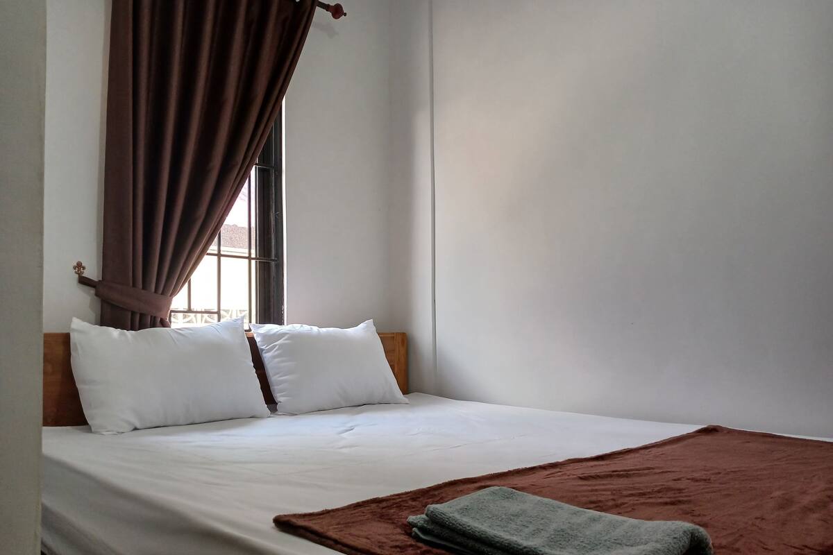 Un lit bien fait, avec des draps blancs, une couverture marron et une serviette pliée.