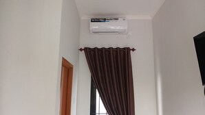 Une pièce avec un climatiseur fixé au plafond, une fenêtre avec un rideau marron et une porte en bois.