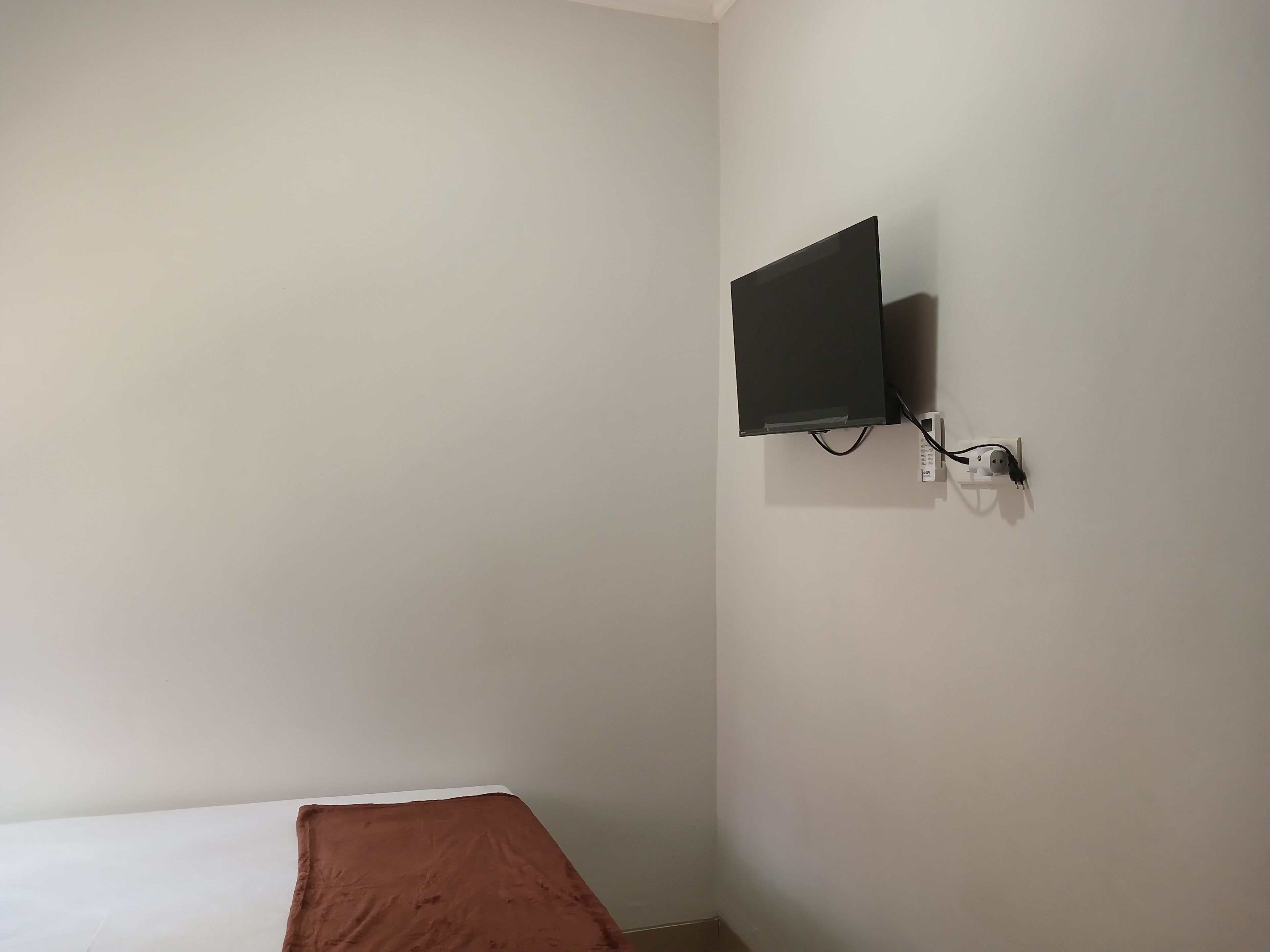 Una habitación con una cama, un televisor de pantalla plana montado en la pared y un enchufe.